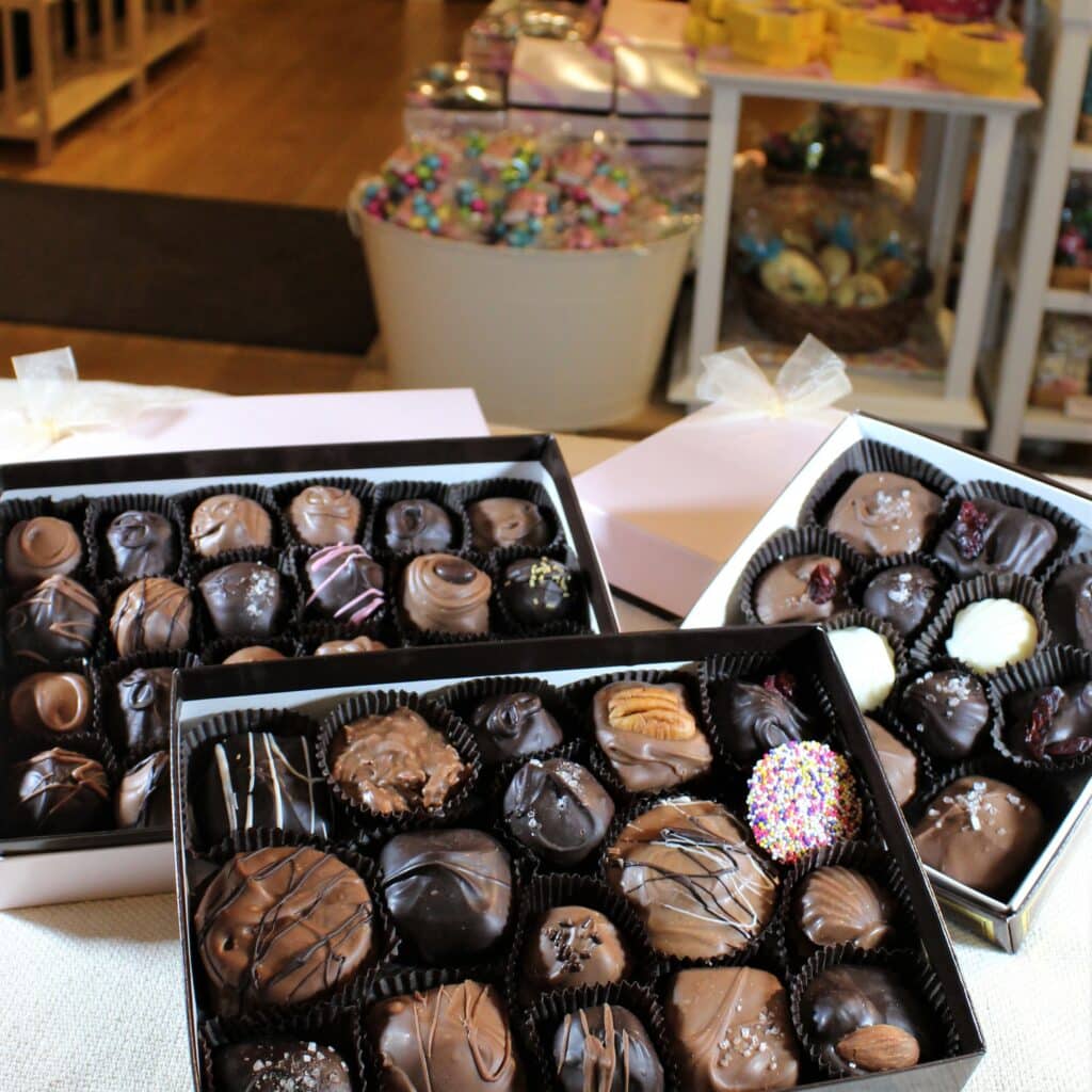 An assortment of elegant chocolates arranged in three boxes, with colorful confections visible in the background.